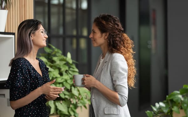 Two women speak to each other in an outdoor area with plants.