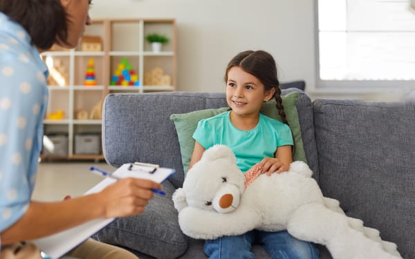 A therapist speaks to a child patient sitting on a couch.