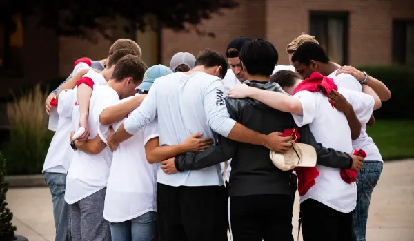 A group of students stand together in a circle in prayer.