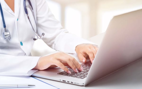 A nurse in a lab coat types on a laptop.