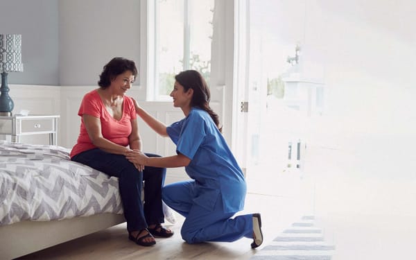 A nurse kneels in front of a patient to console her.