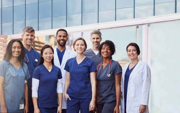 A group of nurses stand side-to-side outside a hospital building.