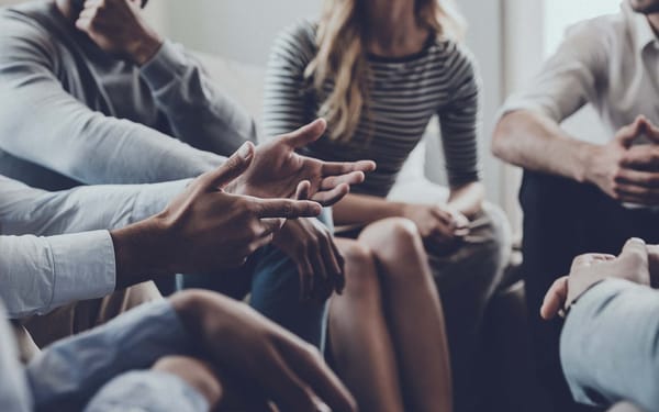 A group of people sit together in a circle during a therapy session.