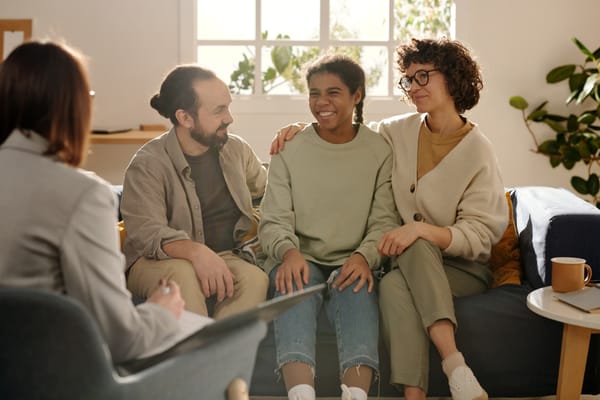 Parents sitting on couch with adopted daughter while talking to social worker. 